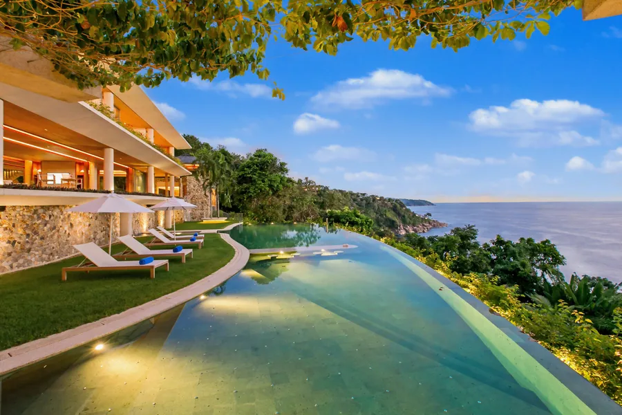 Curved infinity pool at dusk with Villa Cascade lit above and the Andaman Sea beyond, Kamala, Phuket